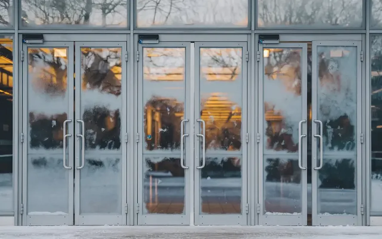 Commercial glass entrance doors with metal frames and frosted windows during winter weather.