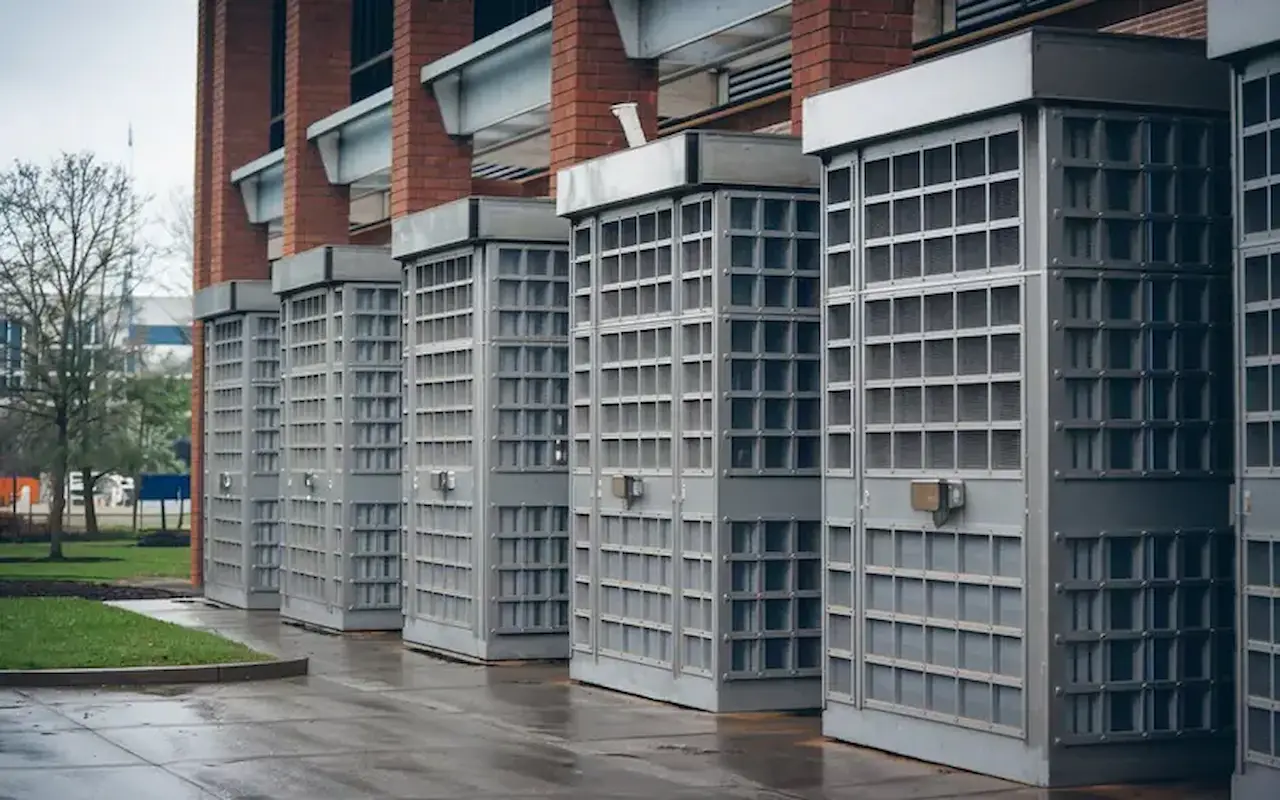 Row of commercial metal security grilles and ventilation enclosures along a modern brick building exterior.