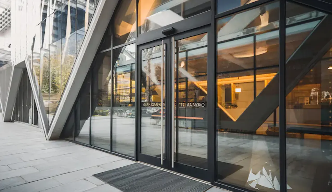 Modern commercial building entrance featuring glass double doors, floor-to-ceiling windows, and contemporary architecture.