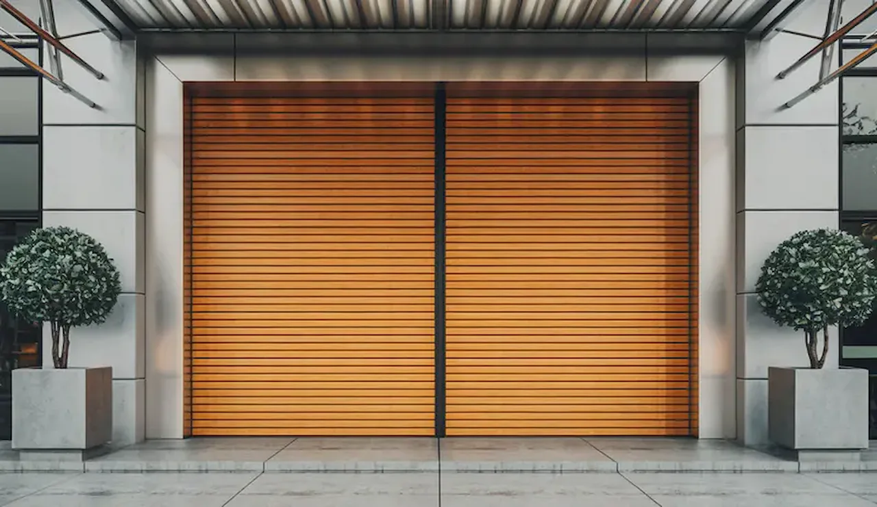 Modern commercial storefront with a closed rolling security door and decorative exterior planters.