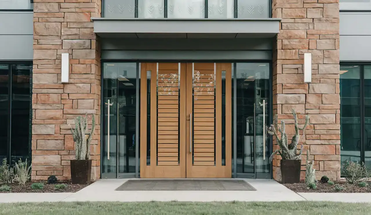 Modern commercial building entrance featuring wood-framed glass doors, stone façade, and landscaped entryway.