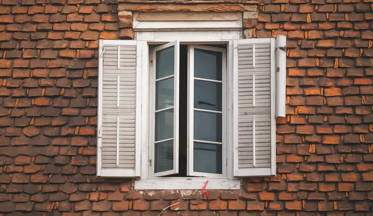 White-framed window with open shutters set in a rustic brick exterior wall.