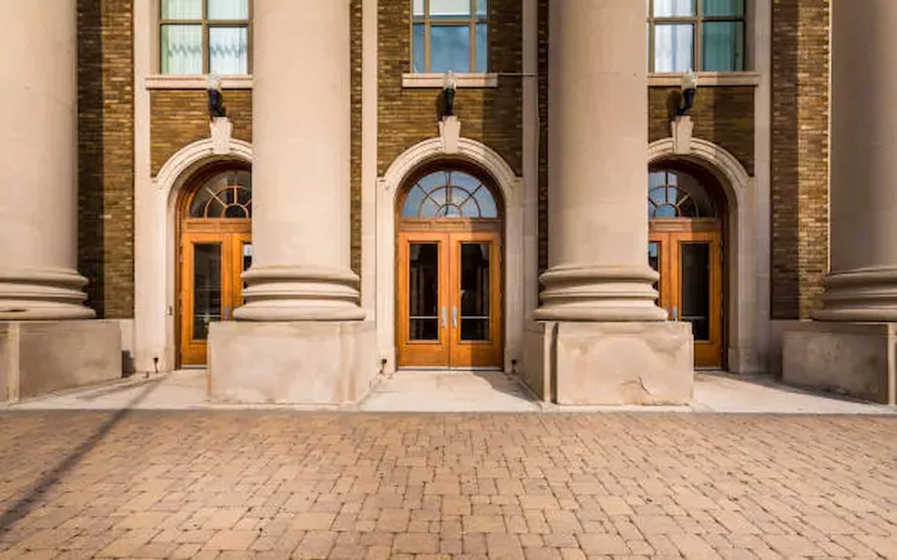 "Grand commercial building entrance featuring tall stone columns, arched transom windows, and wooden double doors in a classical architectural design."