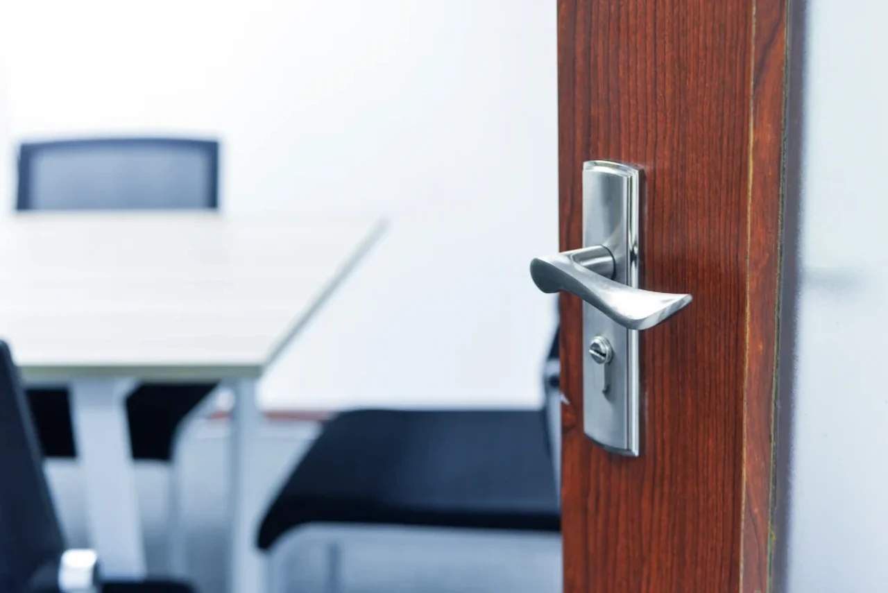 Close-up of a commercial office door with a modern silver lever handle, leading into a clean conference room with chairs and a meeting table in the background.