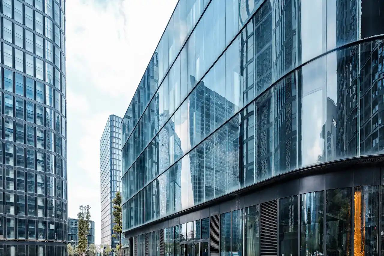 Modern commercial office building with a glass façade reflecting nearby skyscrapers in a contemporary business district.